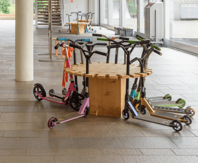 Innenansicht Schulhaus mit einem runden Holzgestell, an dem die Schüler und Schülerinnen ihre Tret-Roller parken können.